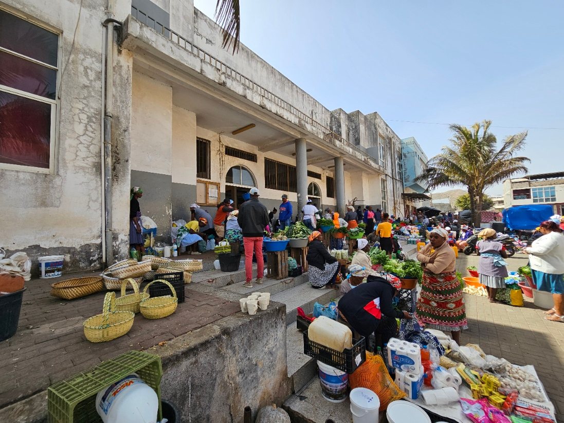 Traders and shoppers beside vegetables, woven baskets and produce outside Assomada market