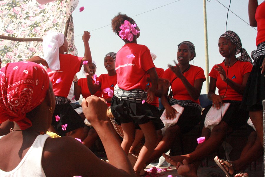 Batukaderas Delta Cultura singing and playing percussion pads around a dancer, wearing red shirts and patterned cloths