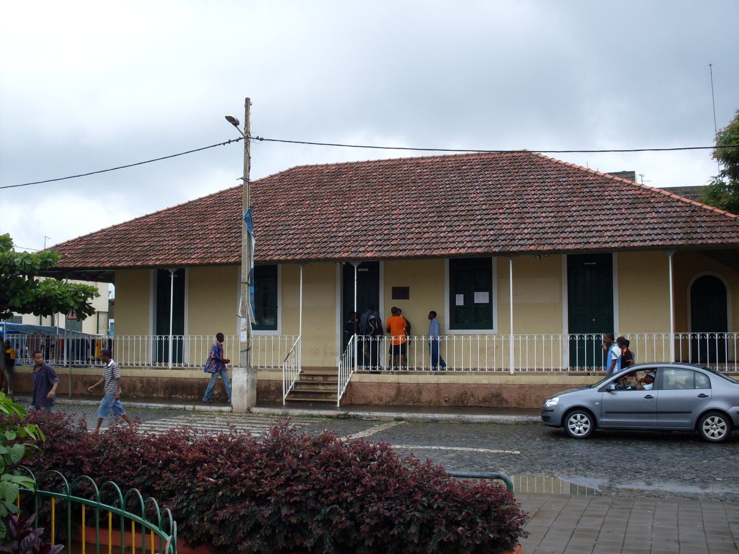 A long tiled-roof building with a covered veranda and people outside, photographed in Assomada