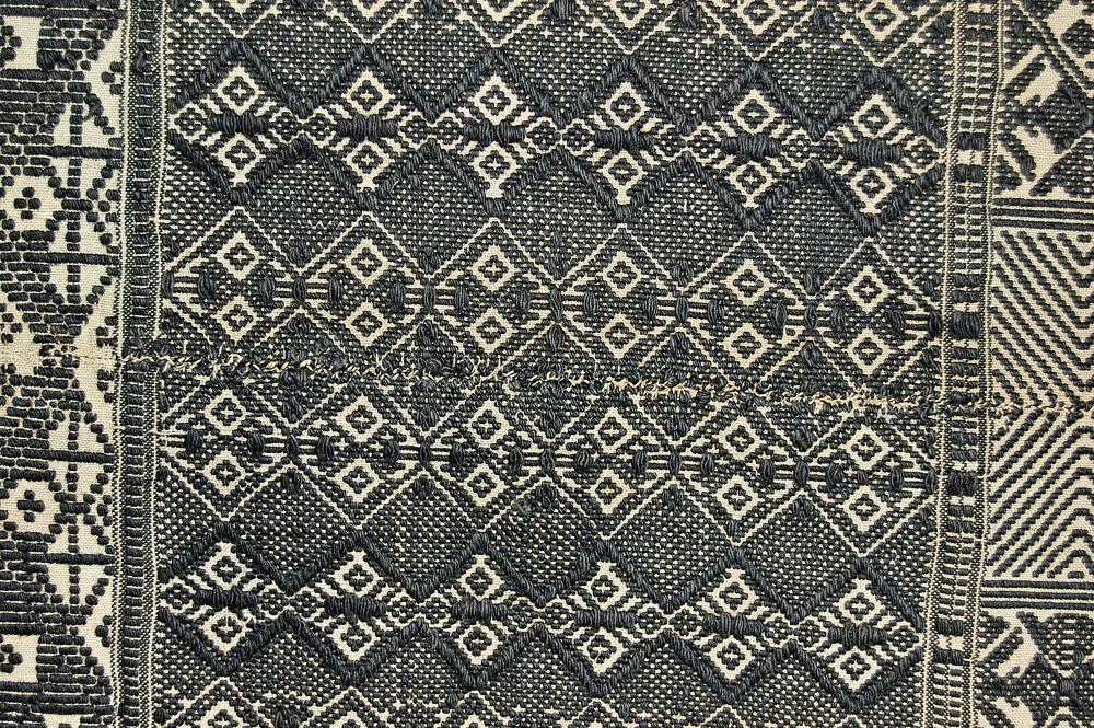 Close detail of the panu d’obra showing dense black and cream diamonds, stepped motifs, raised supplementary weft, and a hand-sewn join between strips